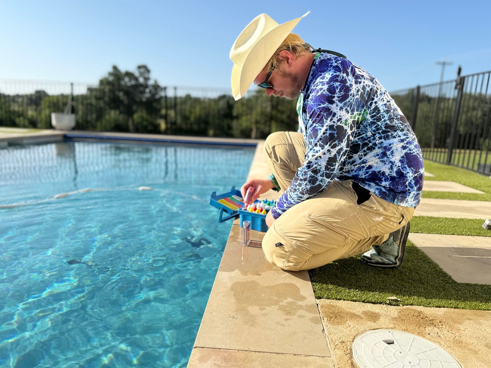 Man in cowboy hat tests pool water near a pool with blue water on a sunny day.