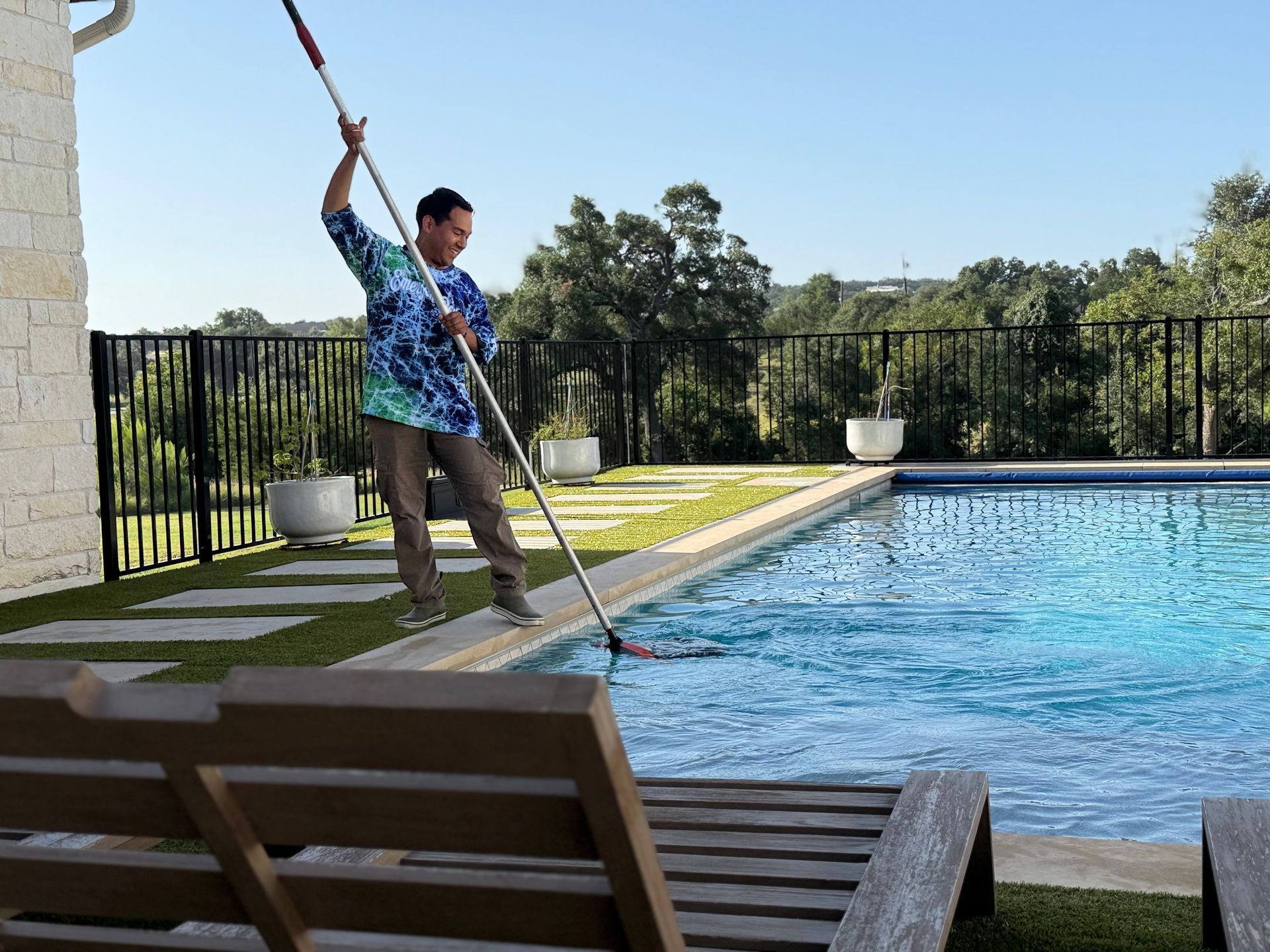 Man cleaning a pool with a net, sunny day, green lawn.
