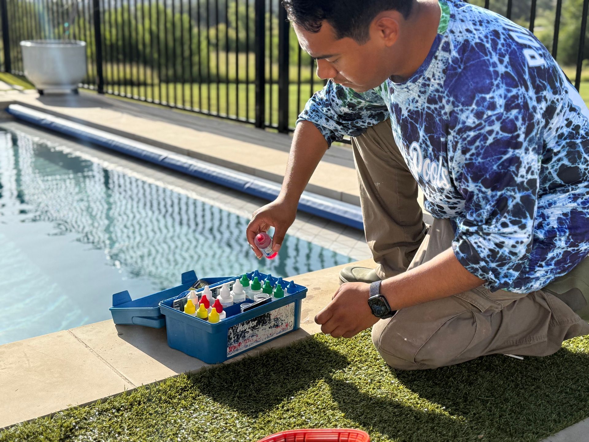 Man testing pool water with a kit outdoors. He kneels near the pool, holding a vial.