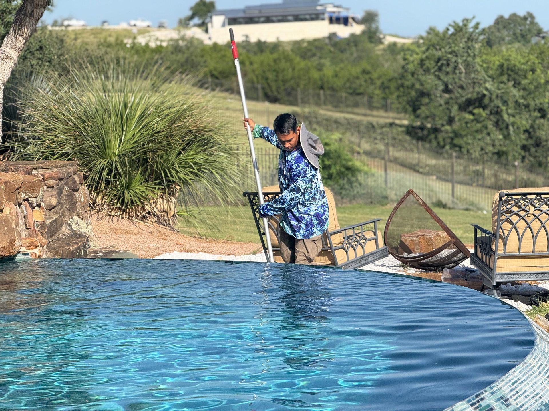 Person in pool cleaning with net and pole, clear blue water, sunny day.