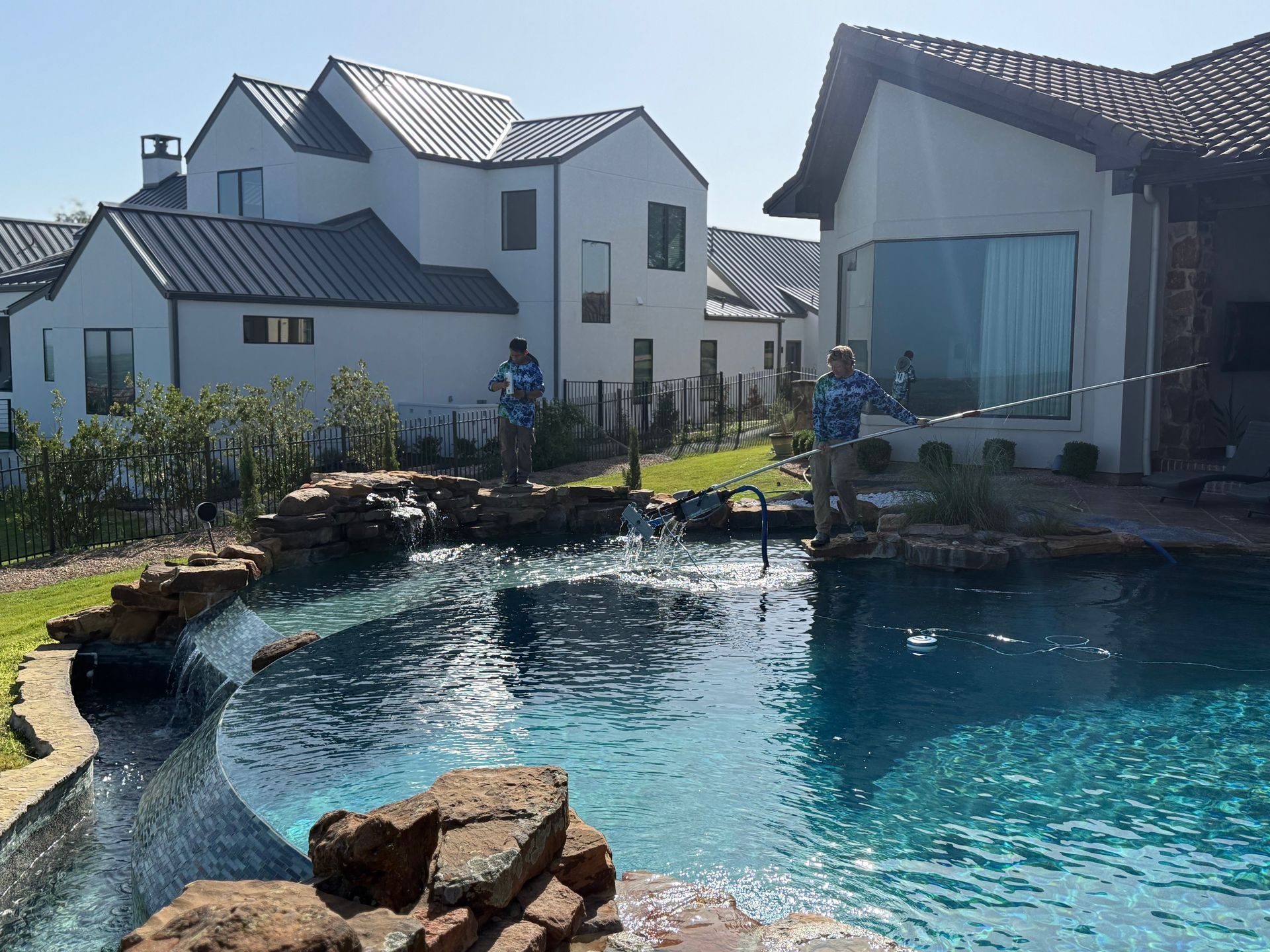 Two people fishing in a pool with waterfalls, next to modern white houses.