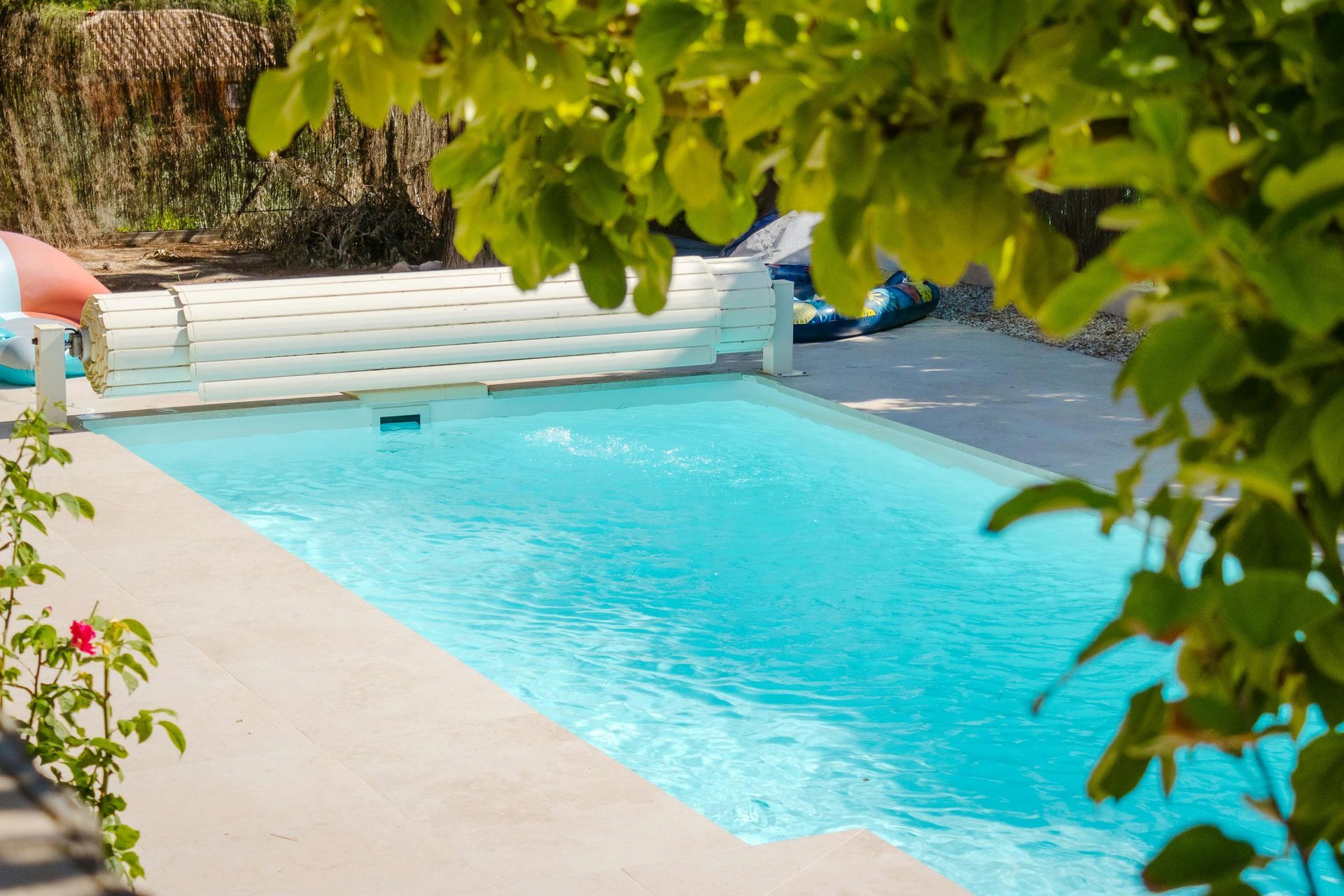Swimming pool with clear blue water, surrounded by a light-colored patio and trees.