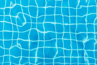 Blue swimming pool with white grid pattern on the bottom, reflecting sunlight.