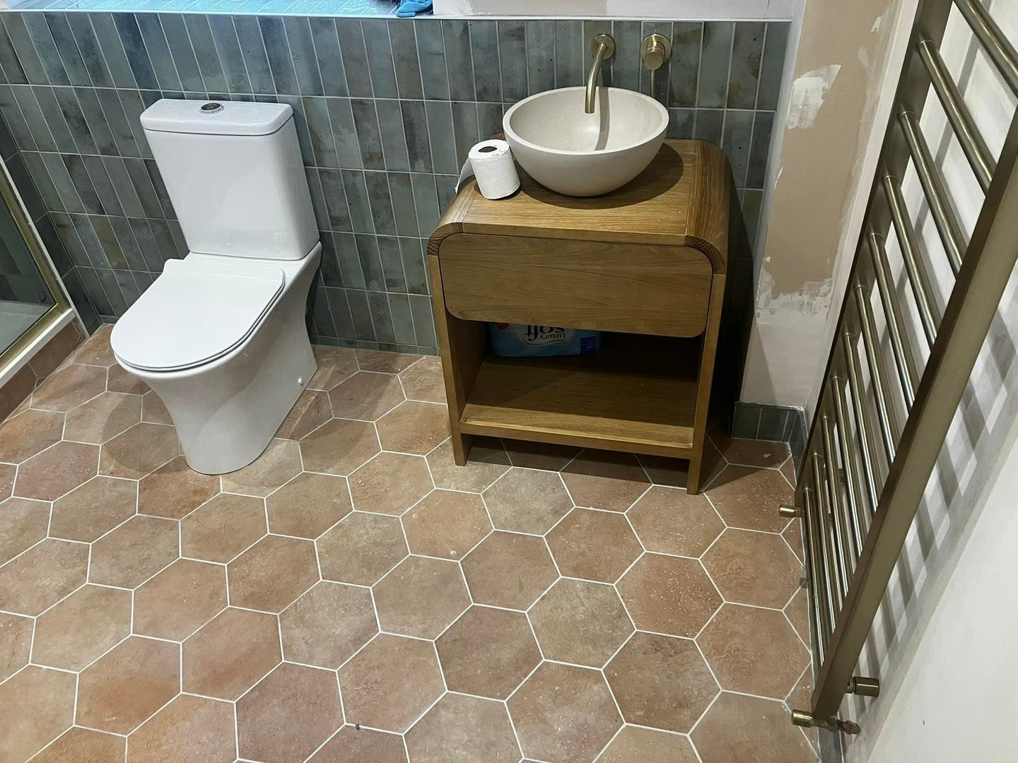 Bathroom with hexagonal floor tiles, toilet, wooden sink vanity, and towel rack.