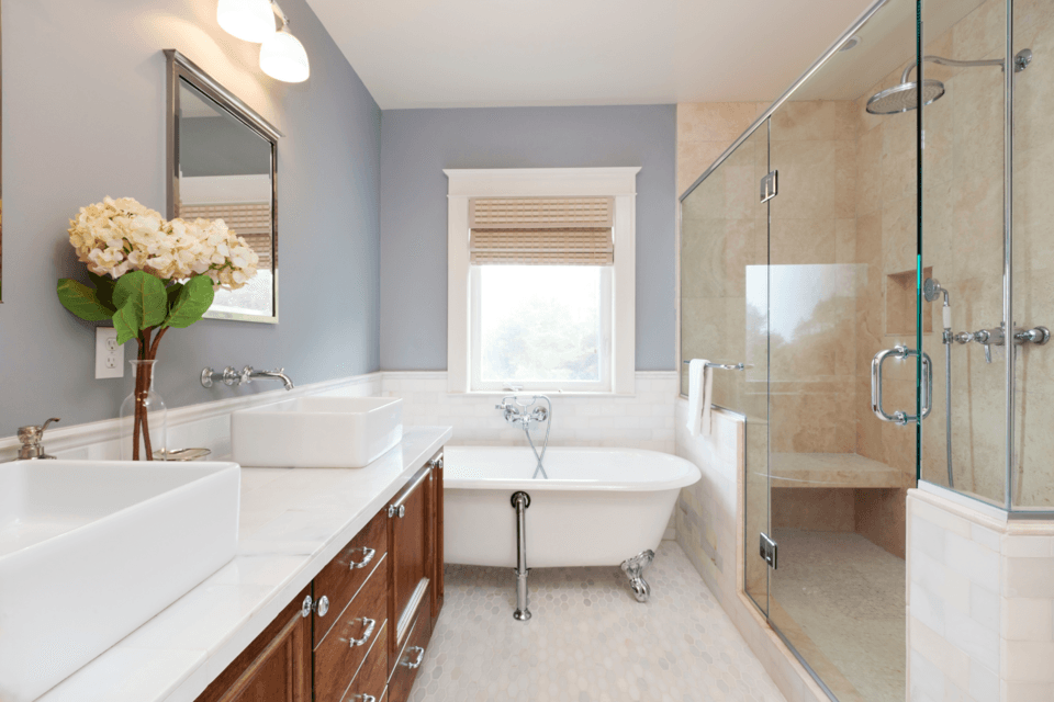 High-end bathroom with a seated shower, free-standing bath and two sinks. The bathroom has a white and brown theme and looks very posh.
