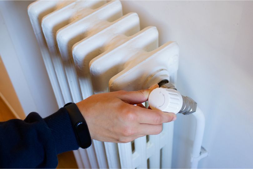 A radiator on the wall that is being turned on, with the gauge turning towards the + sign.