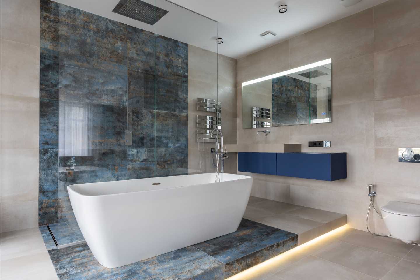 Big freestanding bathtub, walk-in shower and blue tiles in the background, also blue basins, and a large mirror above them.
