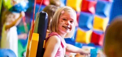 Young child (girl) playing in a park, with paint on her face.