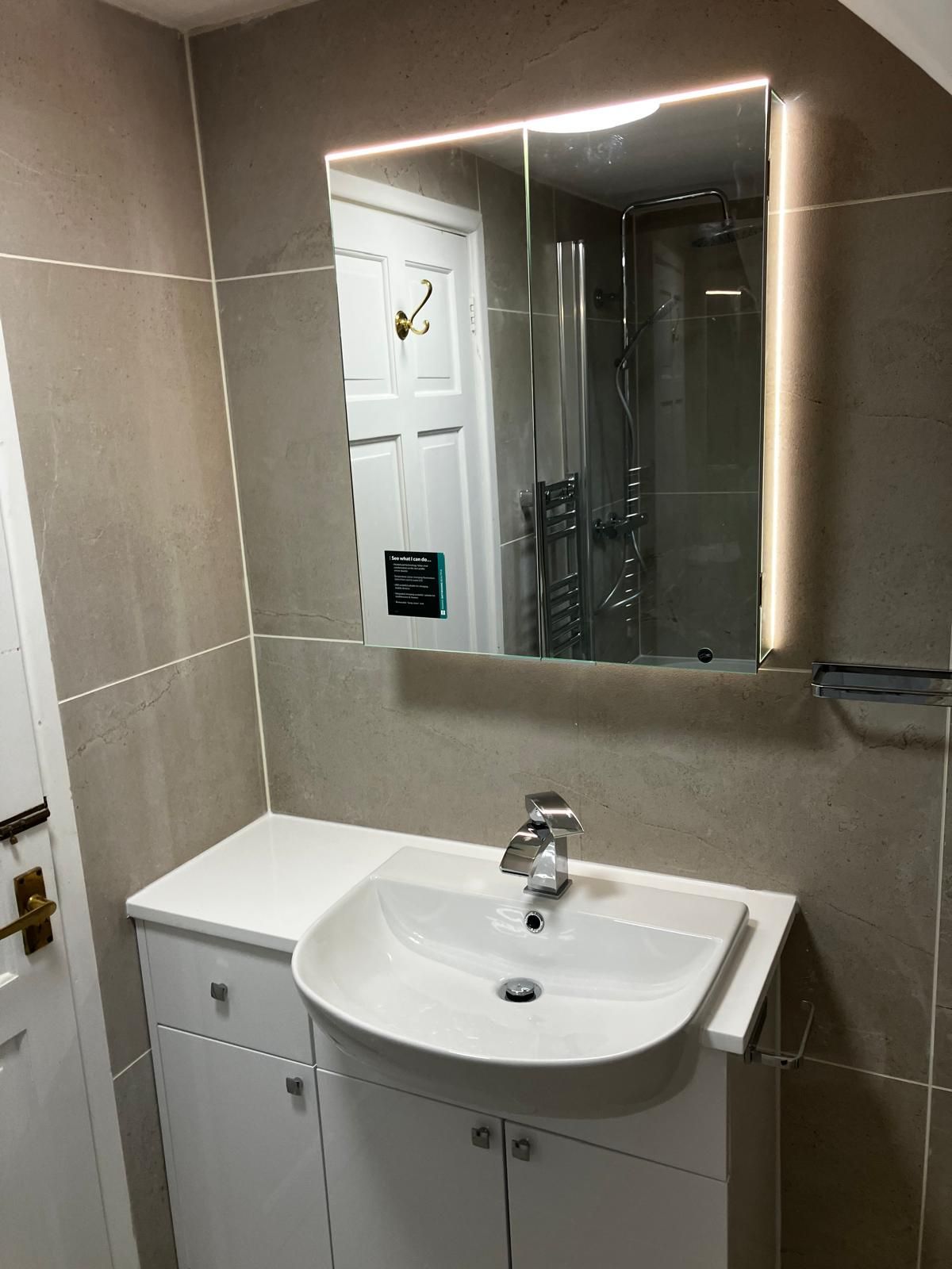 Bathroom with white vanity, sink, and mirror with LED lighting; beige tiled walls.