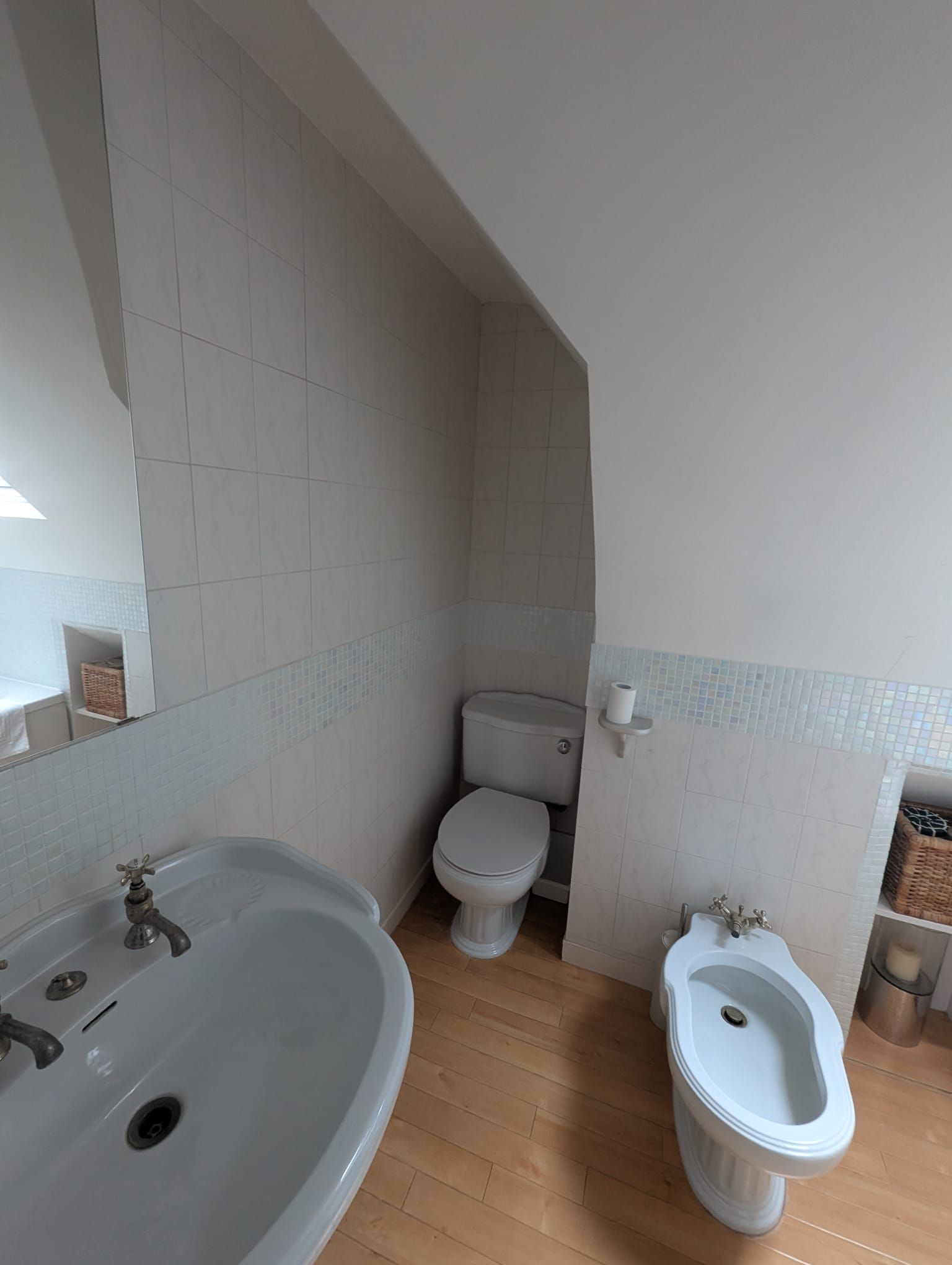 Bathroom with white toilet, bidet, and sink. Wooden floor and tiled walls.