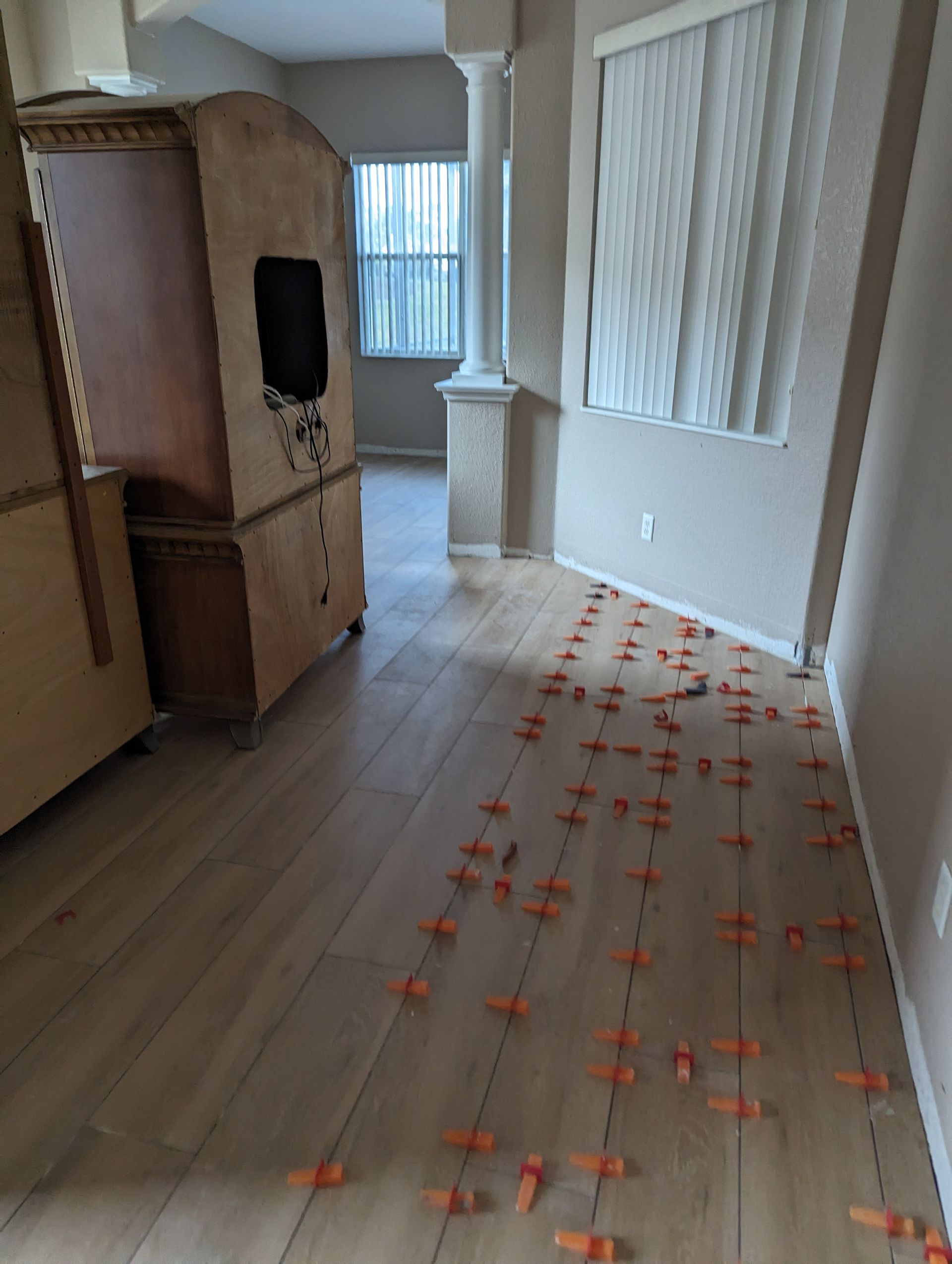 A room with a wooden floor and orange tile spacers on the floor.