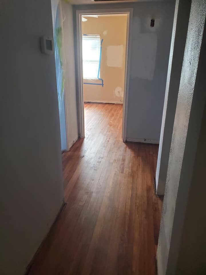 Hallway with wood floor, leading to a room with window. Walls are neutral tones.