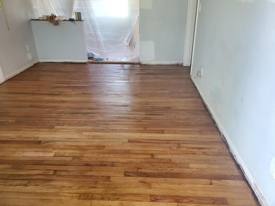 Refinished hardwood floor in a room with light blue walls and a window covered in plastic sheeting.