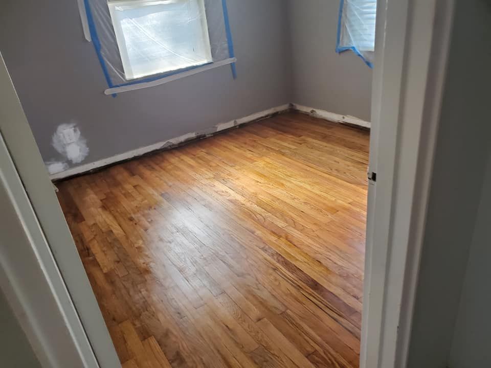 Hardwood floor in a room, with gray walls and a window covered in plastic.