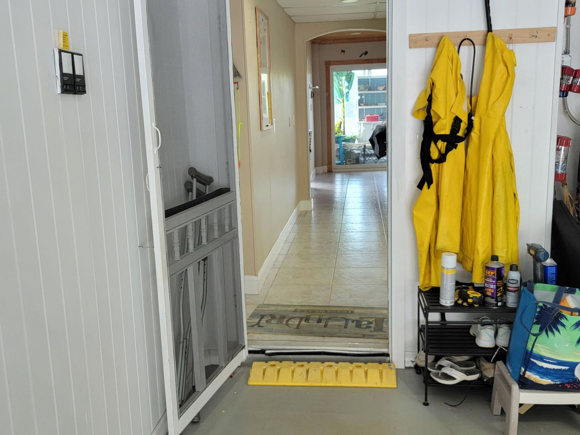 A hallway with a screen door and yellow jackets hanging on hooks