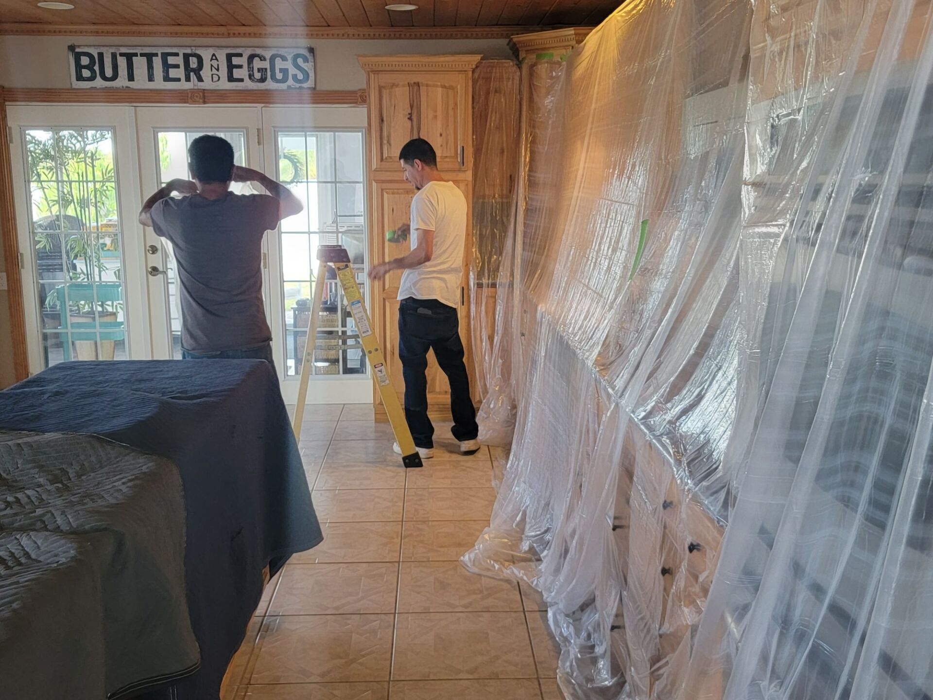 A couple of men are standing in a kitchen covered in plastic.