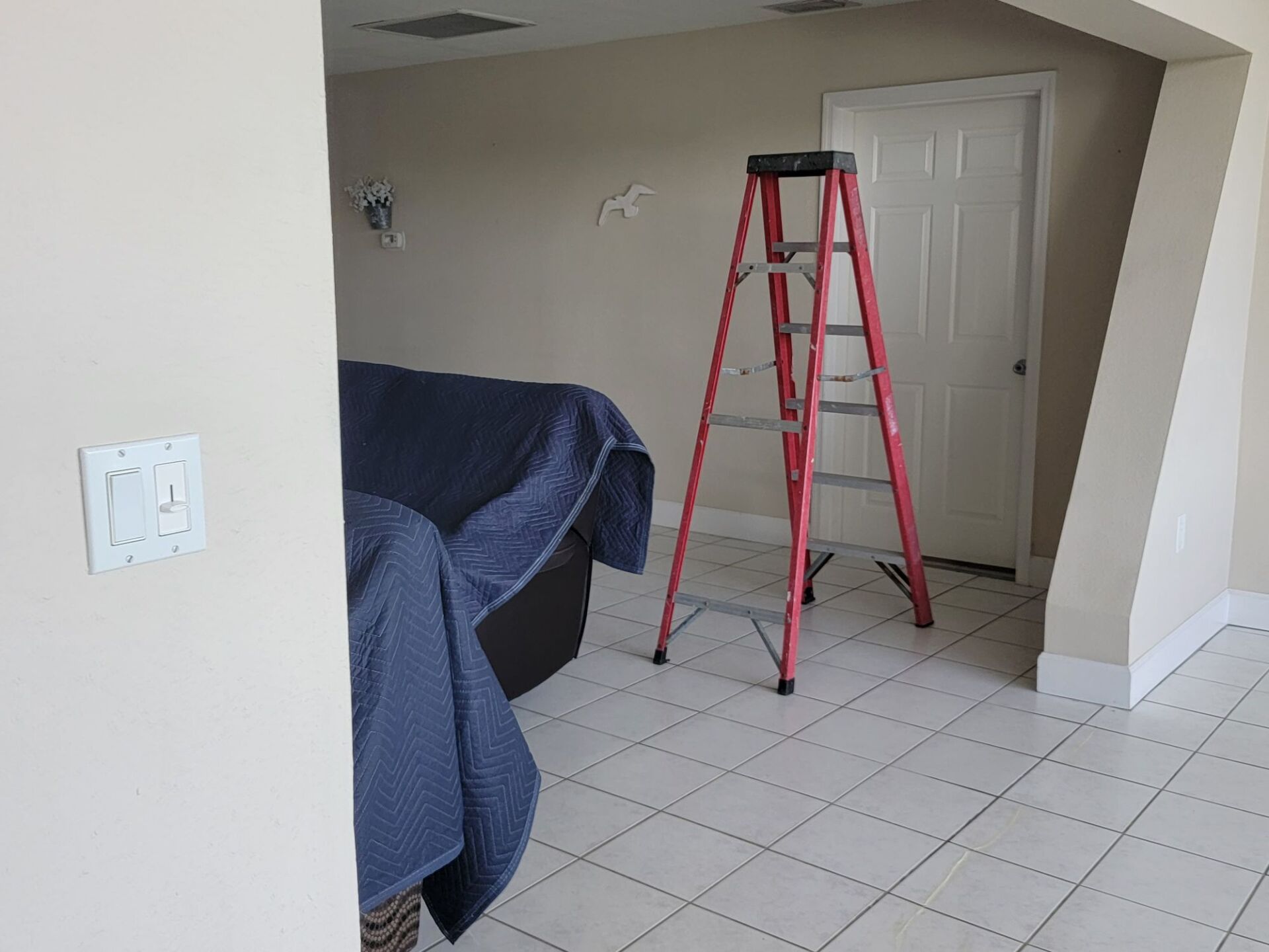 A red ladder is sitting in a room next to a door.