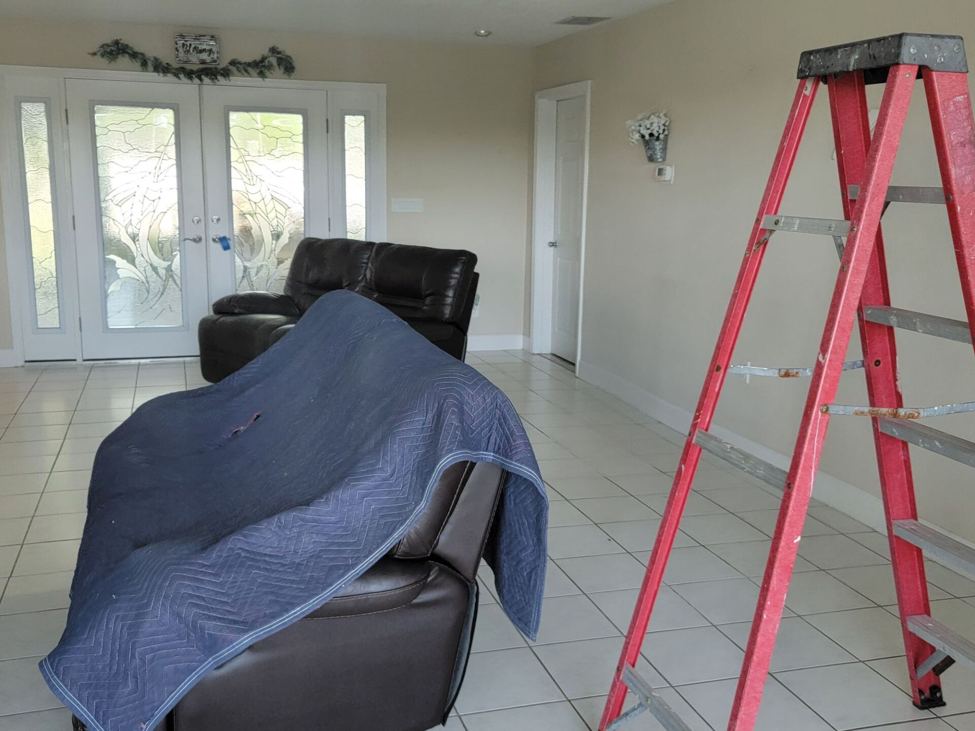 An empty living room with a chair covered in a blue blanket and a red ladder