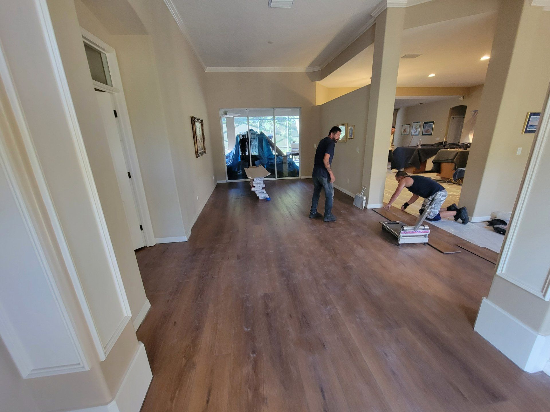 Two men are installing a wooden floor in a living room.