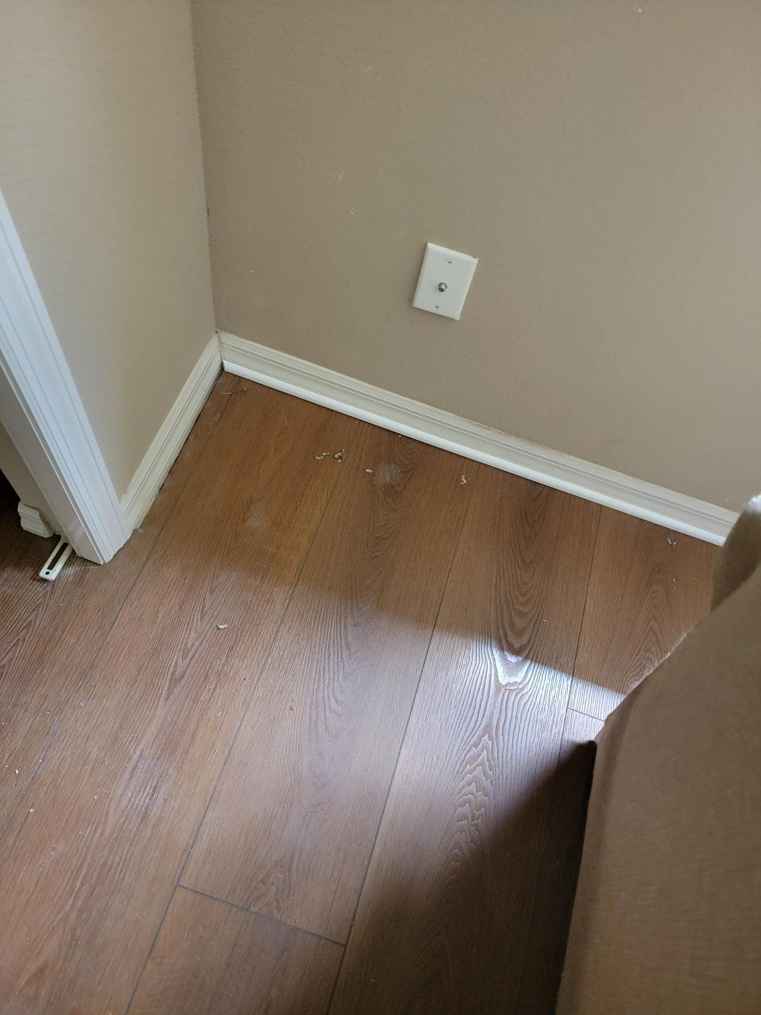 A corner of a room with hardwood floors and a light switch on the wall.
