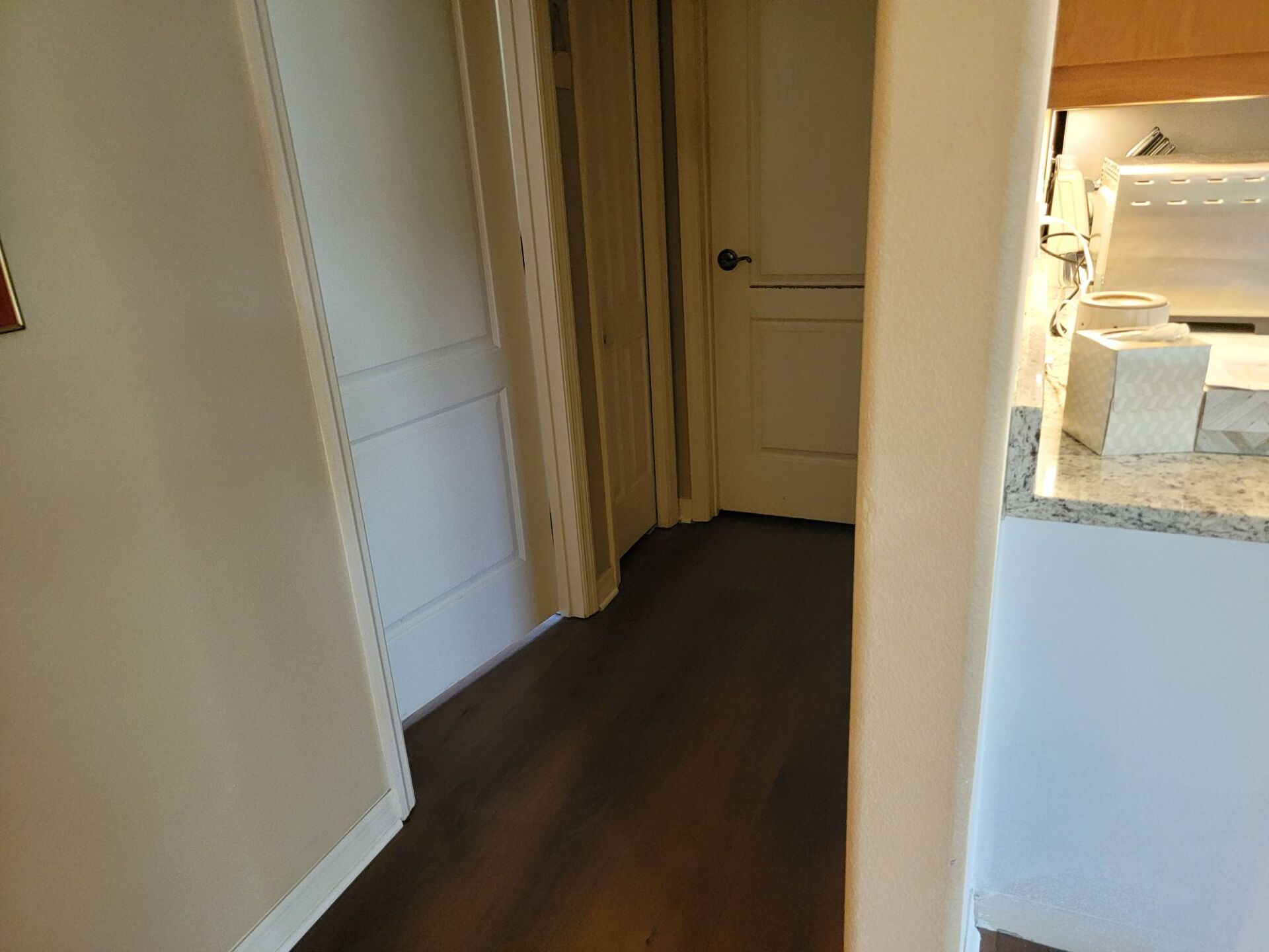 A hallway leading to a kitchen with hardwood floors