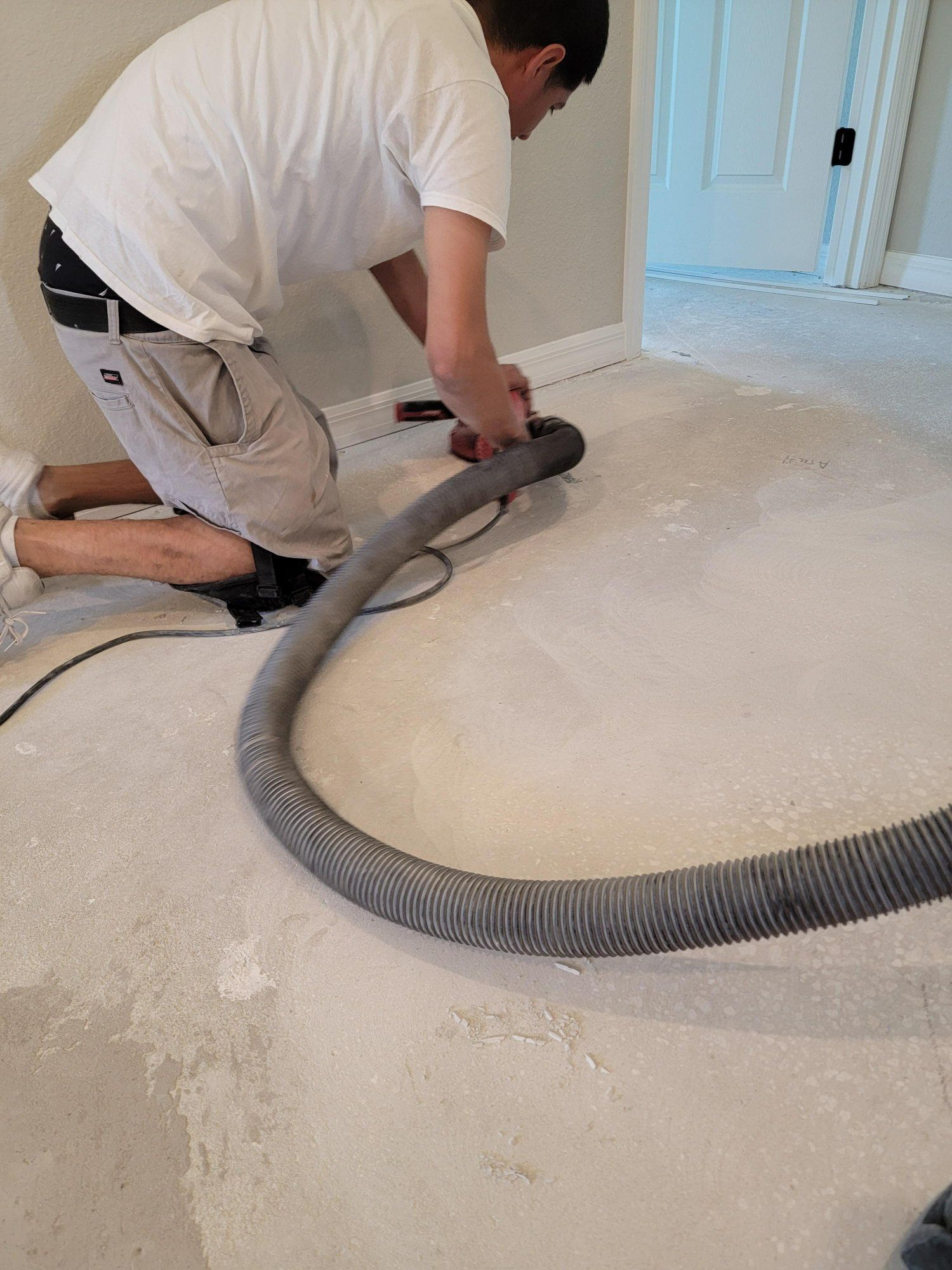 A man is kneeling on the floor using a vacuum cleaner.