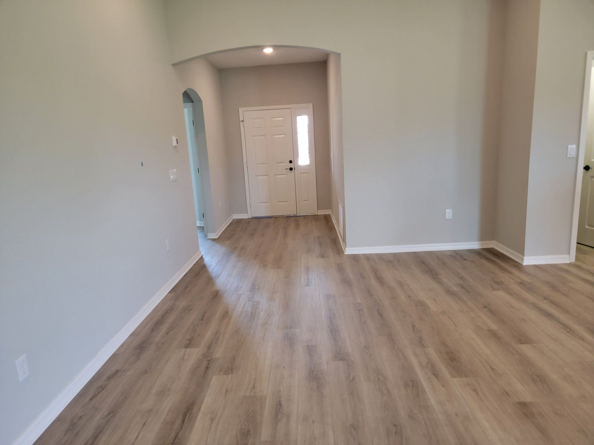 An empty living room with hardwood floors and a white door.