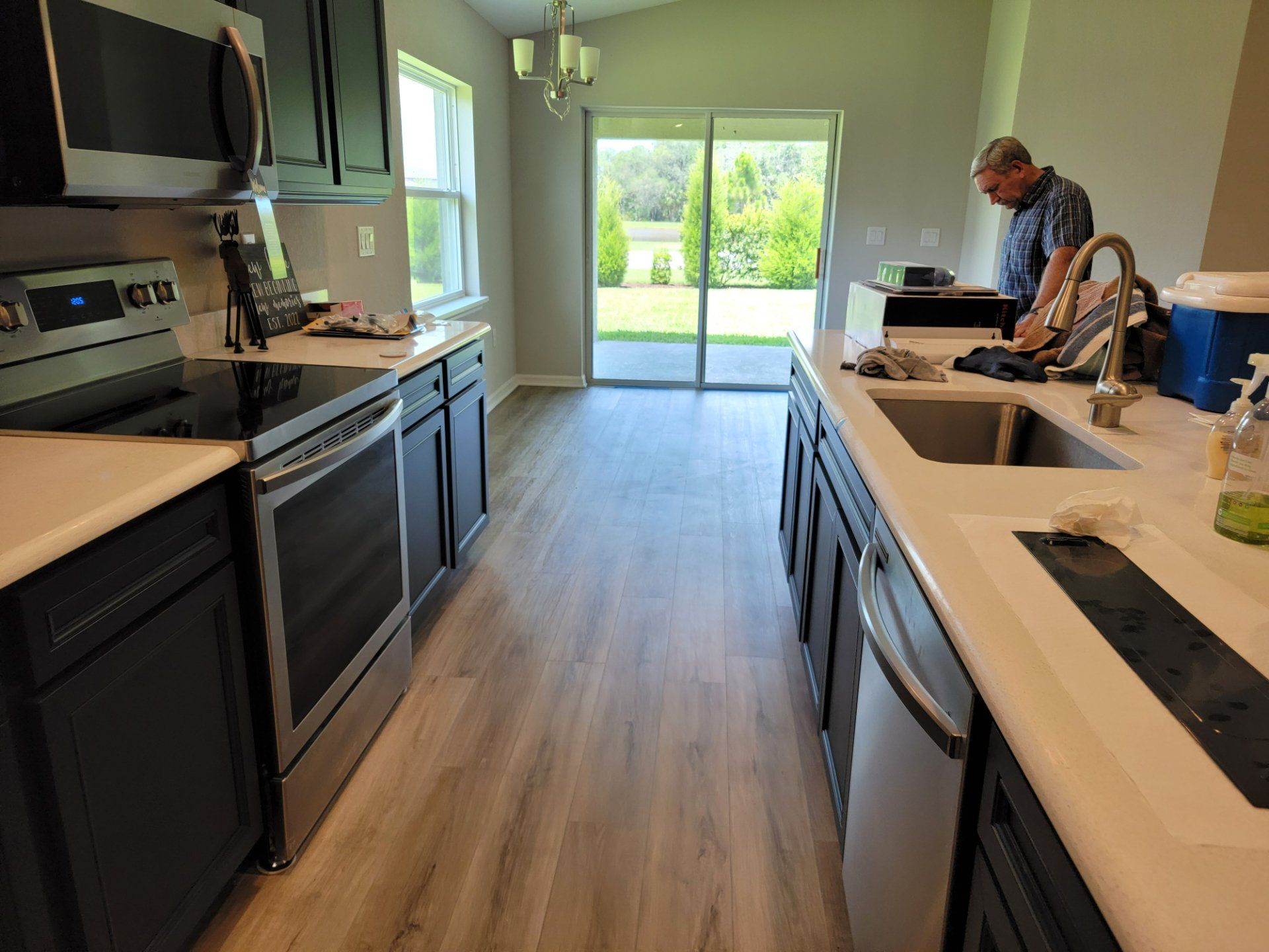 A man is standing in a kitchen next to a sink and stove.