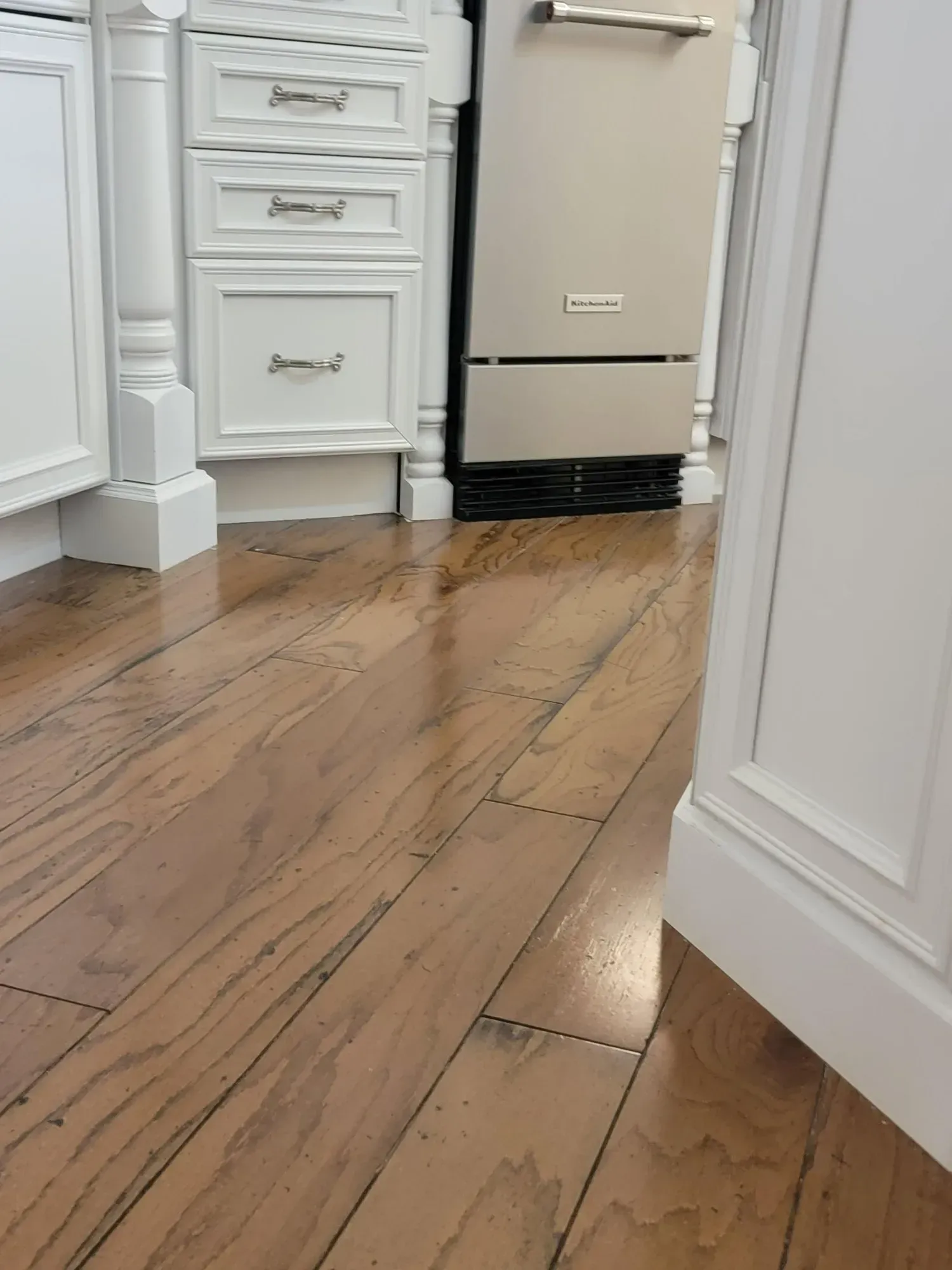 Wood floor in kitchen with white cabinets, silver refrigerator, and molding.
