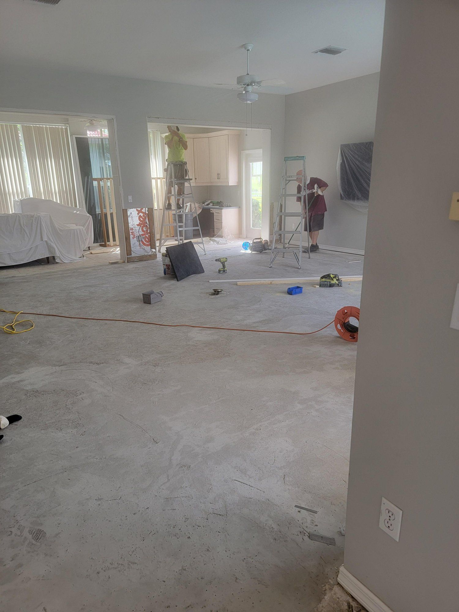 A living room with a carpeted floor and a man standing on a ladder in the background.