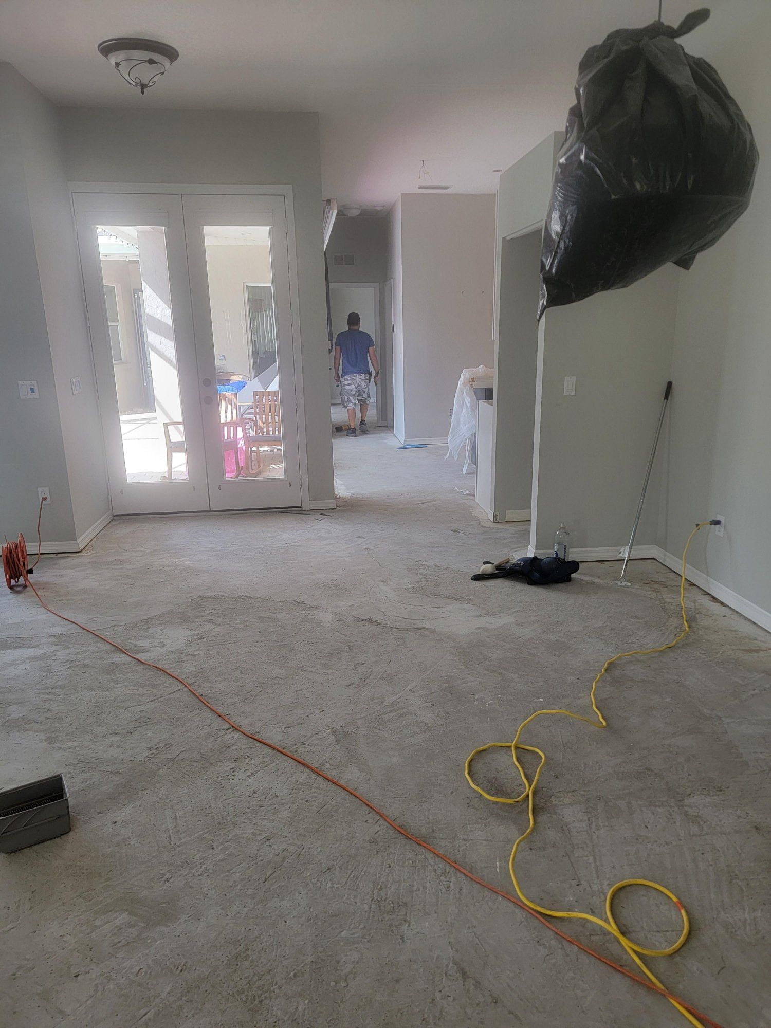 An empty living room with a vacuum cleaner and a trash bag hanging from the ceiling.