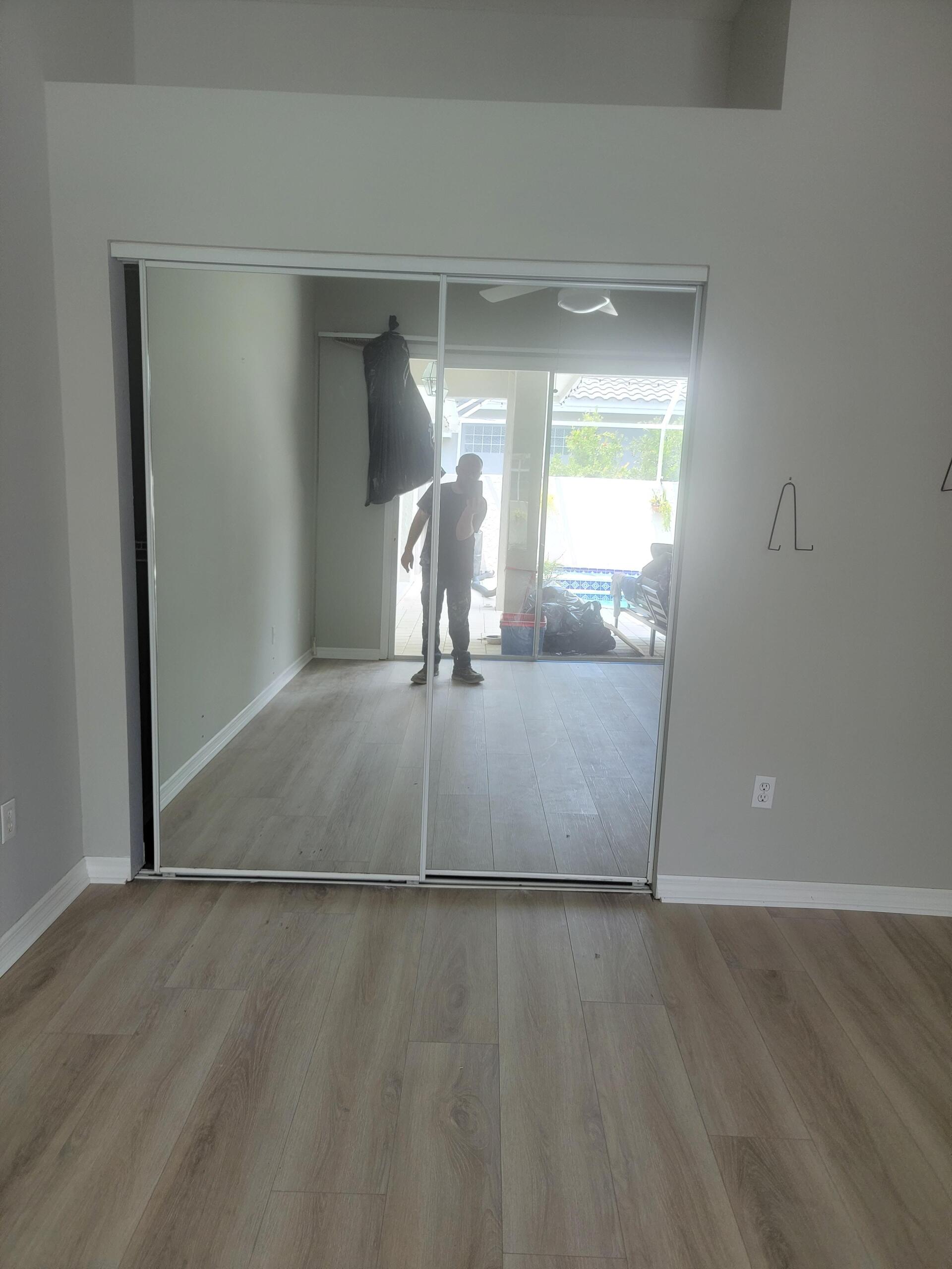 A man is standing in front of a large mirror in an empty room.