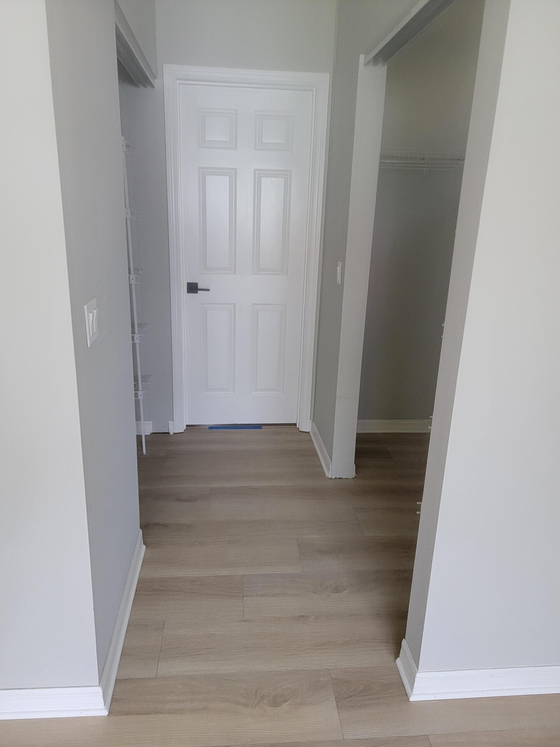 A hallway with hardwood floors and white walls leading to a door.
