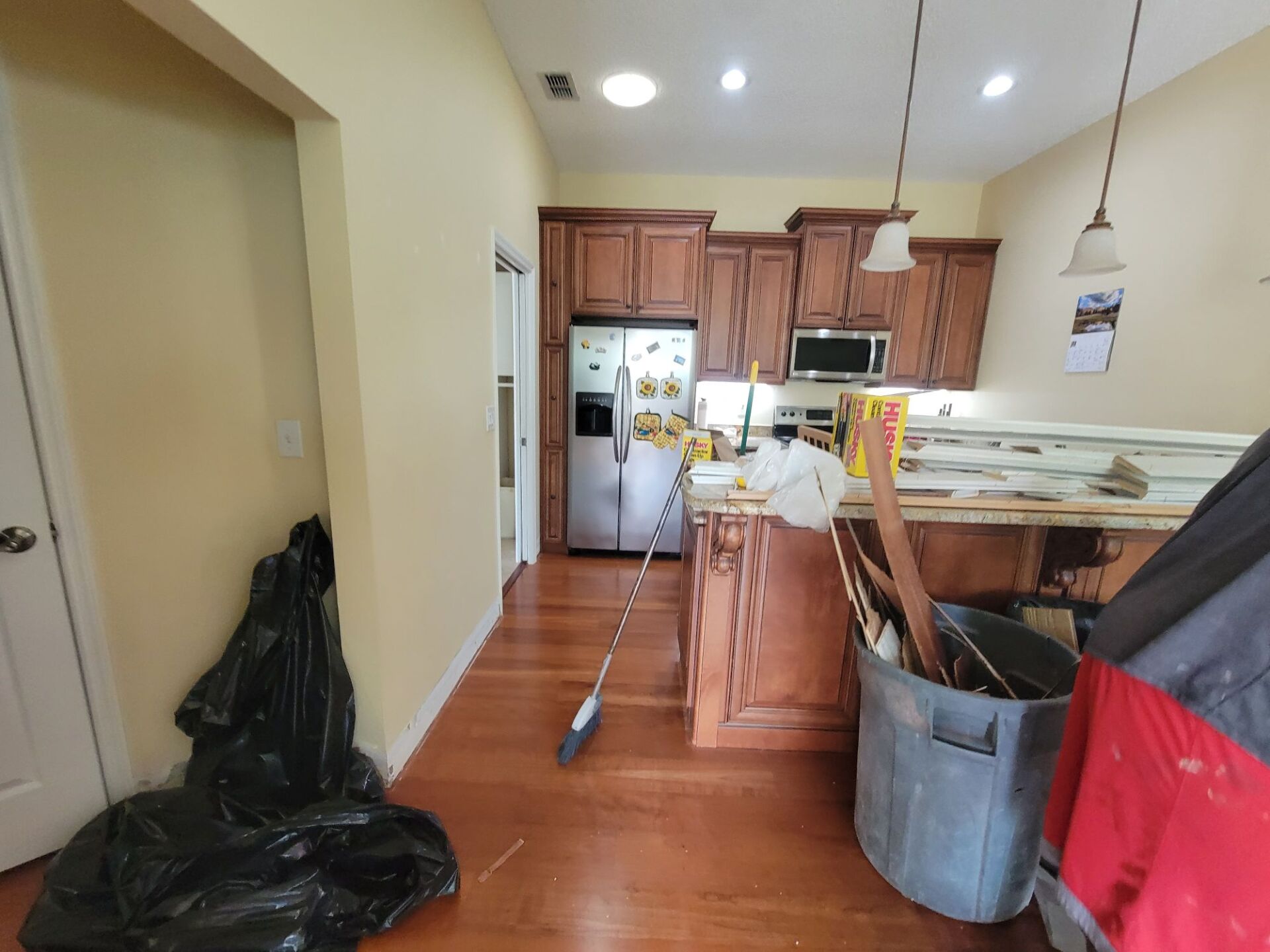 A kitchen with a trash can and a broom on the counter.