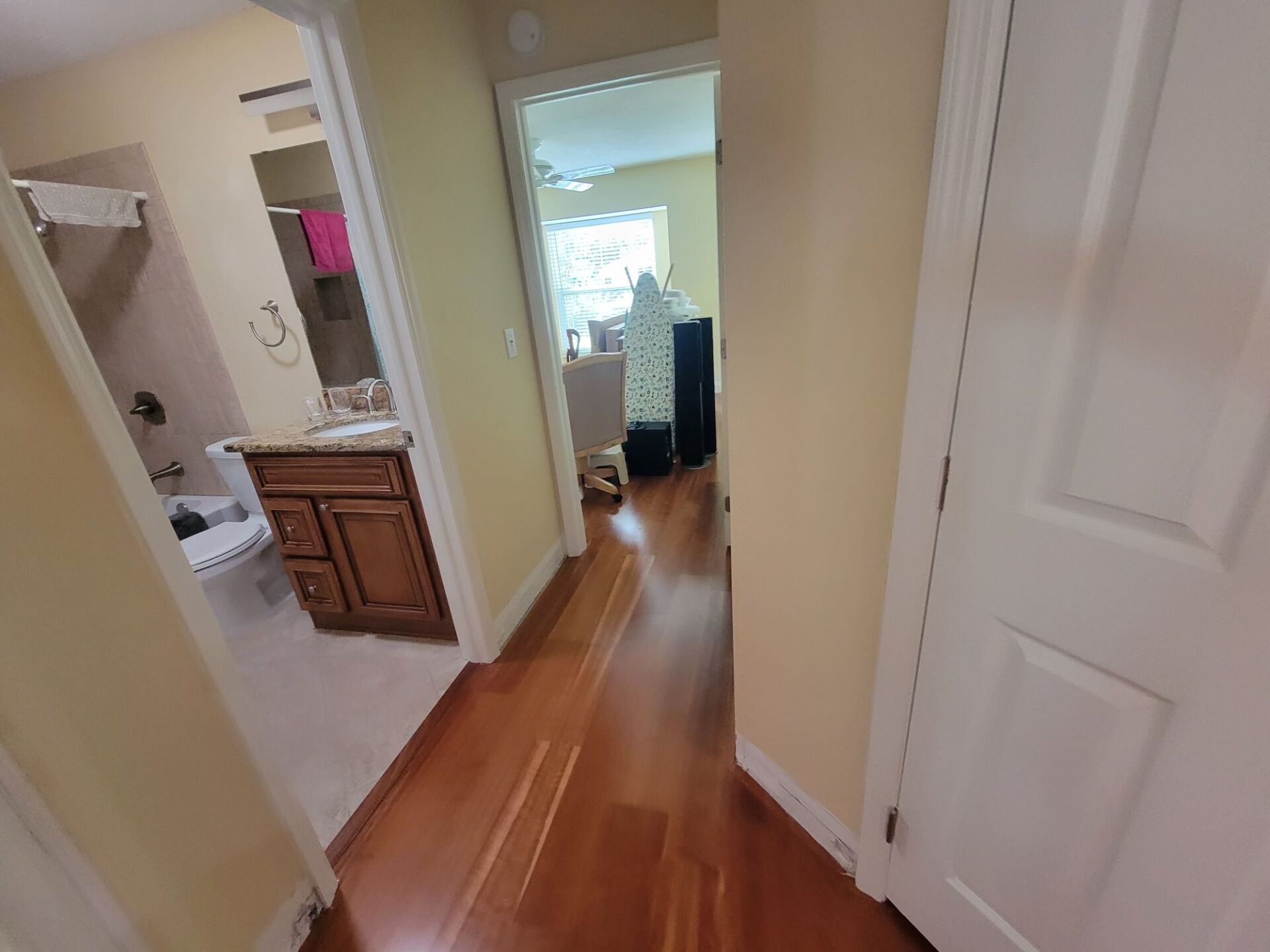 A hallway with hardwood floors leading to a bathroom and a sink.