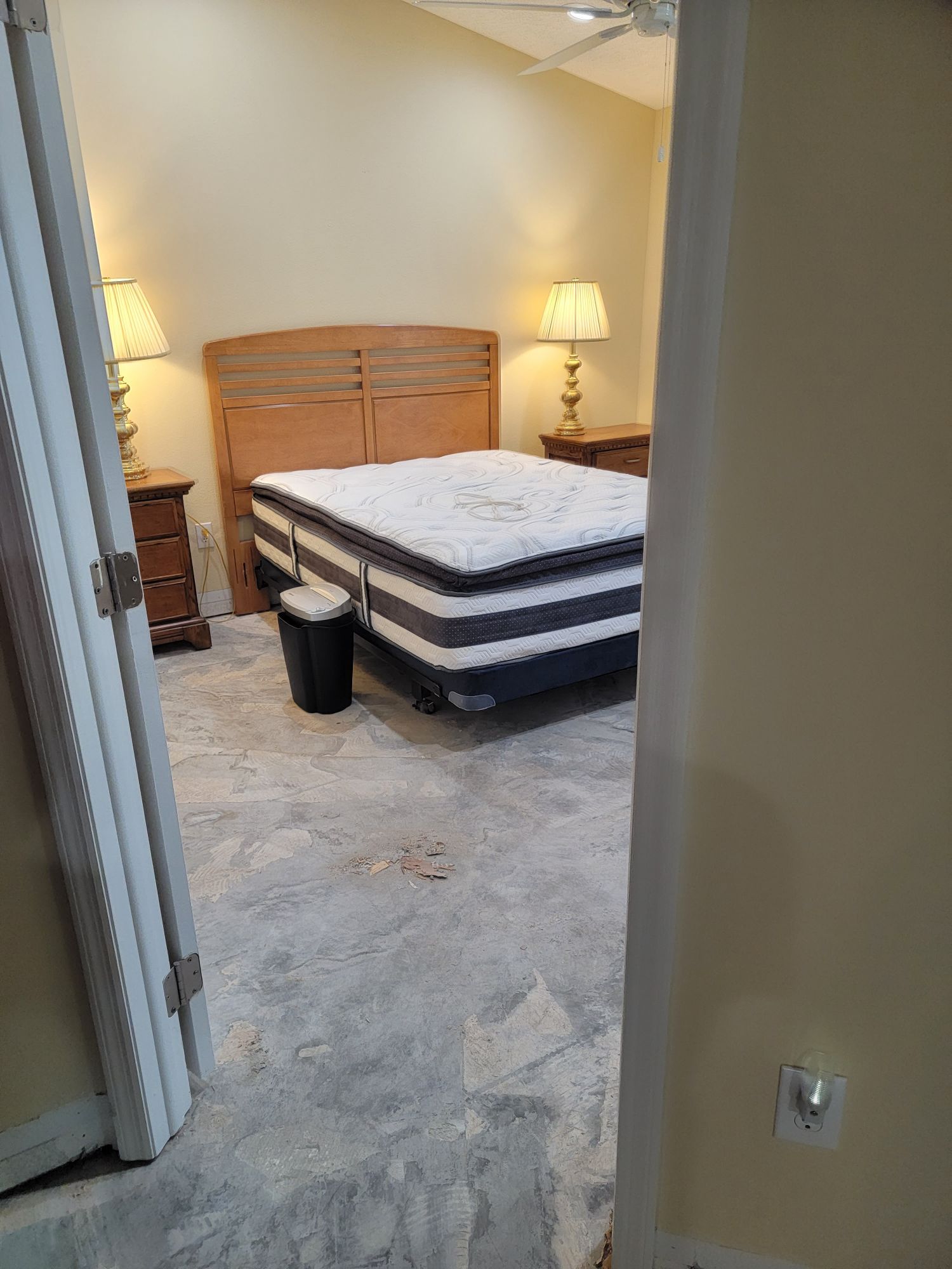 A bedroom with a mattress and a trash can in it.