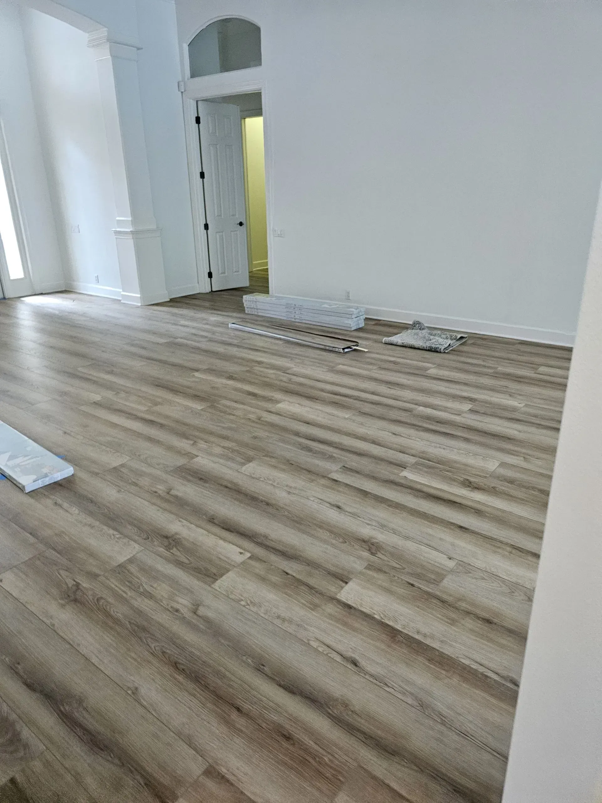 Wooden floor in a room with white walls, doorway, and some flooring materials scattered about.