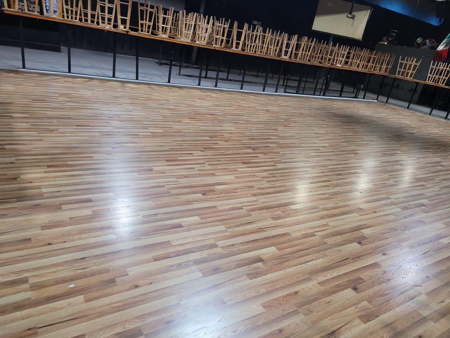 Wooden floor of a roller skating rink, with rows of tables and chairs along the side.