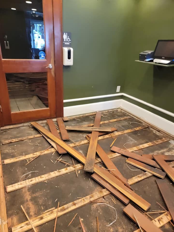 Interior view of a room under construction, with exposed wooden frames and damaged walls. Light gray flooring.