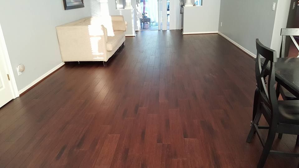 Woman in dark uniform smiles, holds papers, stands near indoor plants in a hallway.