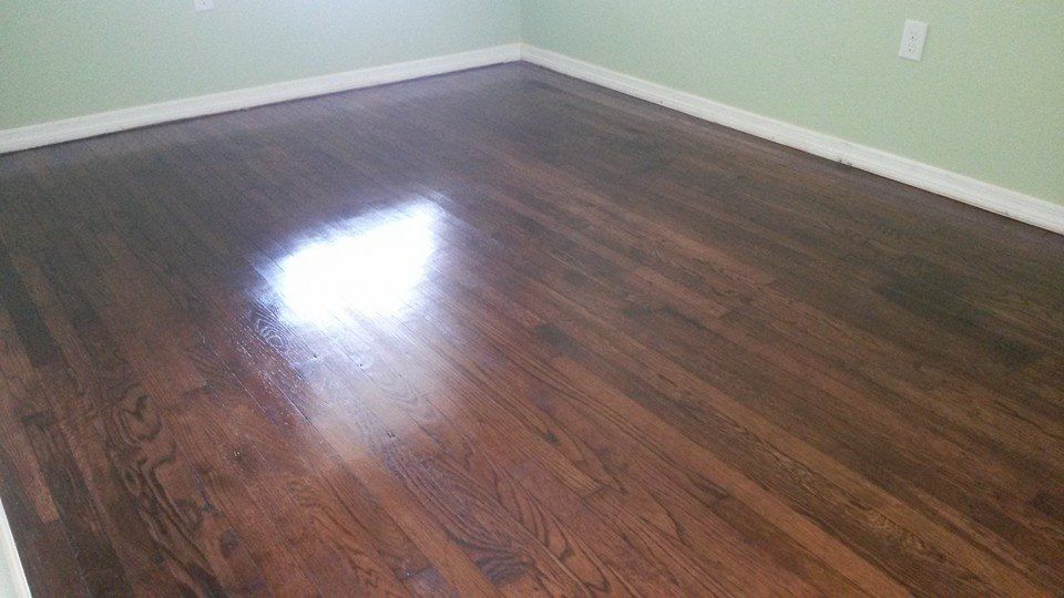 Polished, dark wood floor in a room with light green walls and white baseboards. Bright reflection.