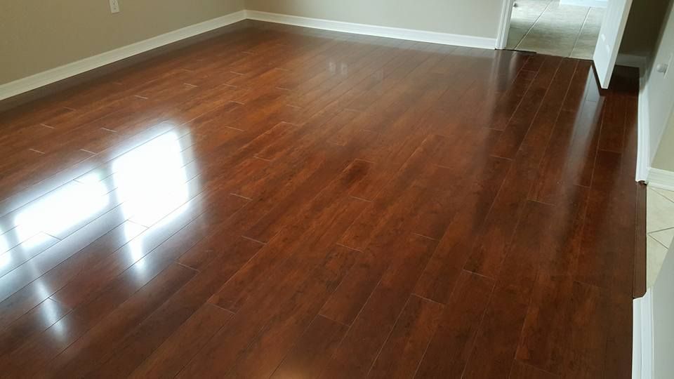 Glossy, dark brown hardwood floor reflecting light from a window, in an empty room.