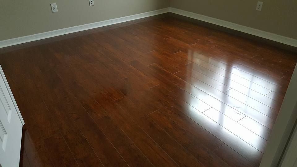 Woman in green uniform smiles, pushing cleaning cart in modern building hallway.