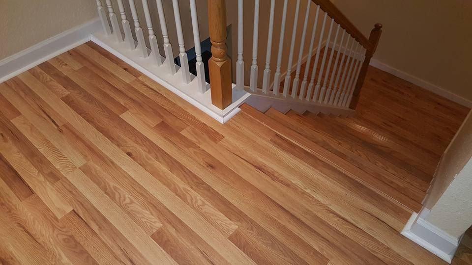 Hardwood floor next to a staircase with white balusters and wooden handrail.