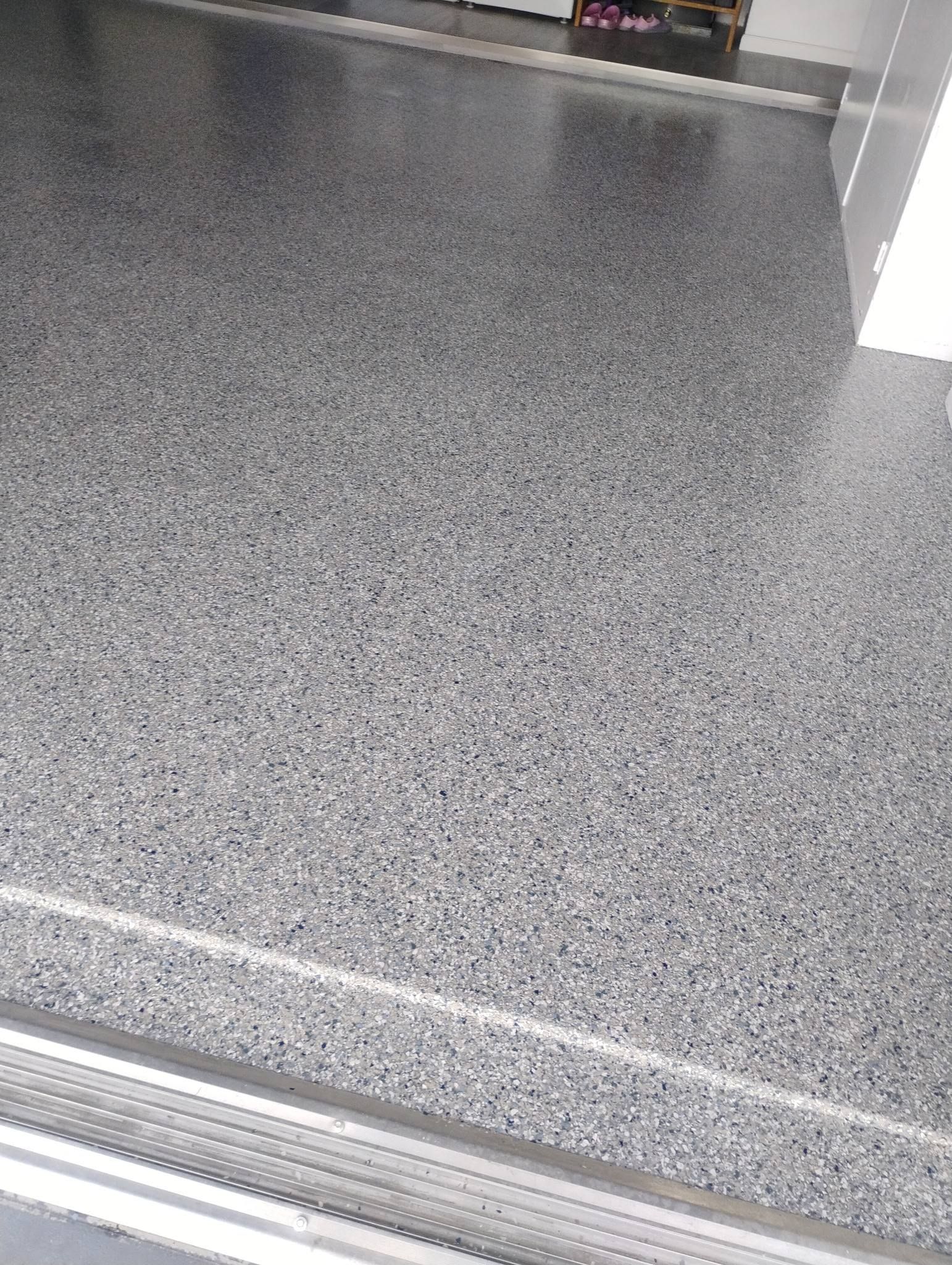 Woman in dark uniform smiles, holds papers, stands near indoor plants in a hallway.