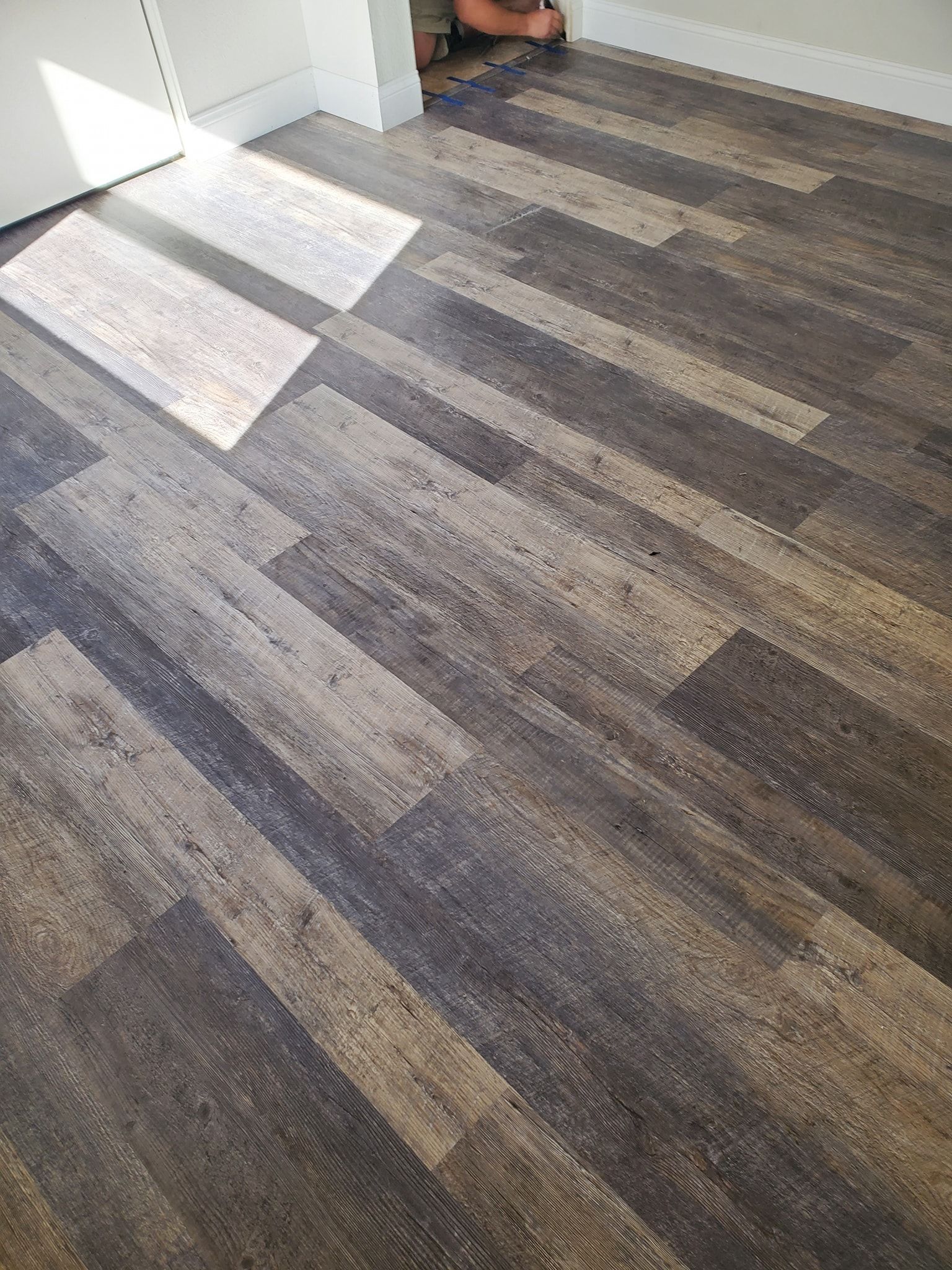 Dark brown wood-look flooring, with sunlight streaming in from the left.