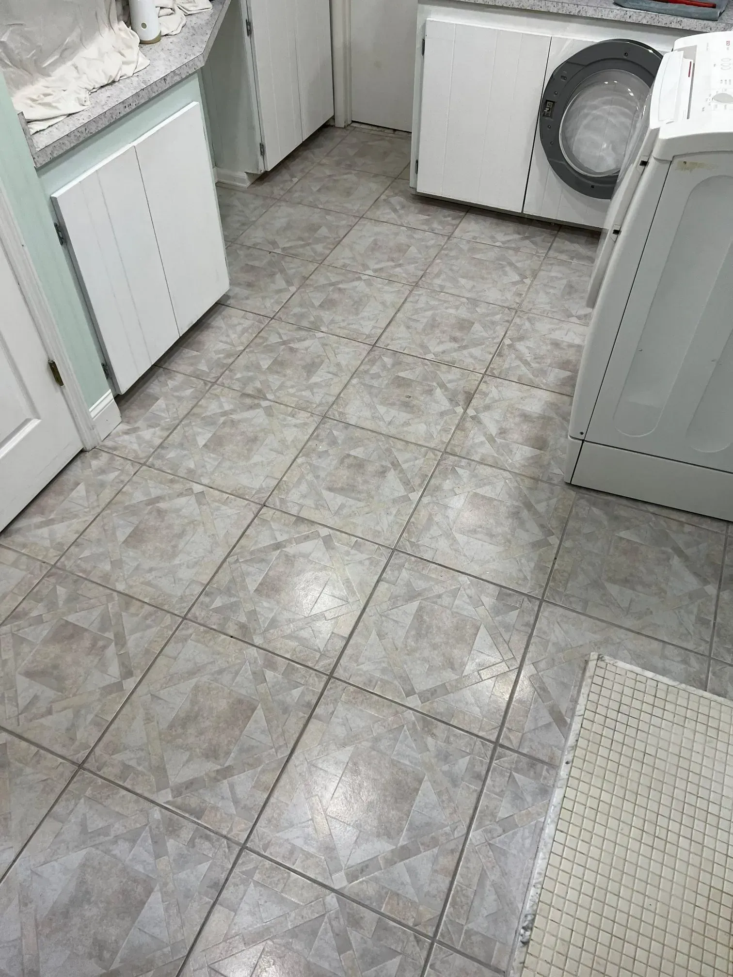 Laundry room with gray and white tile floor. Washing machine, cabinets, and a rug are present.