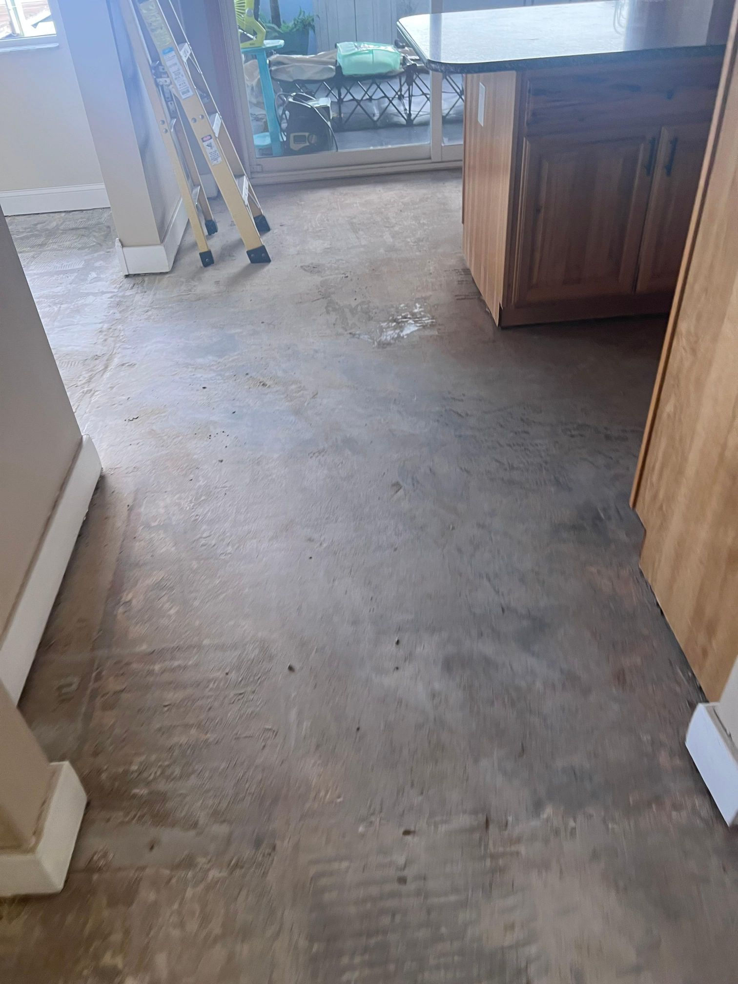 A dirty concrete floor in a kitchen with a ladder in the background.