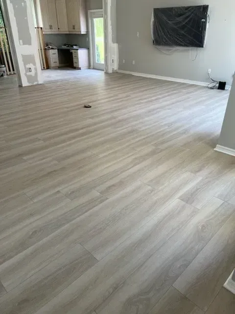 Light wood-look flooring installed in a room. Kitchen cabinets and a television are visible in the background.