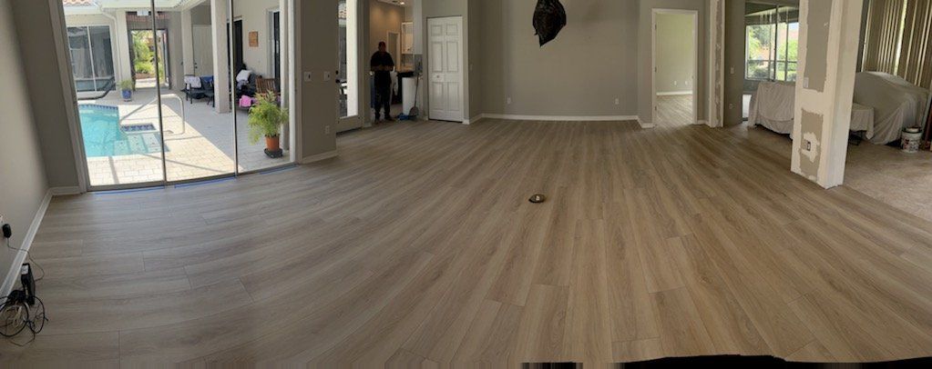 A large empty room with a wooden floor and a pool in the background.